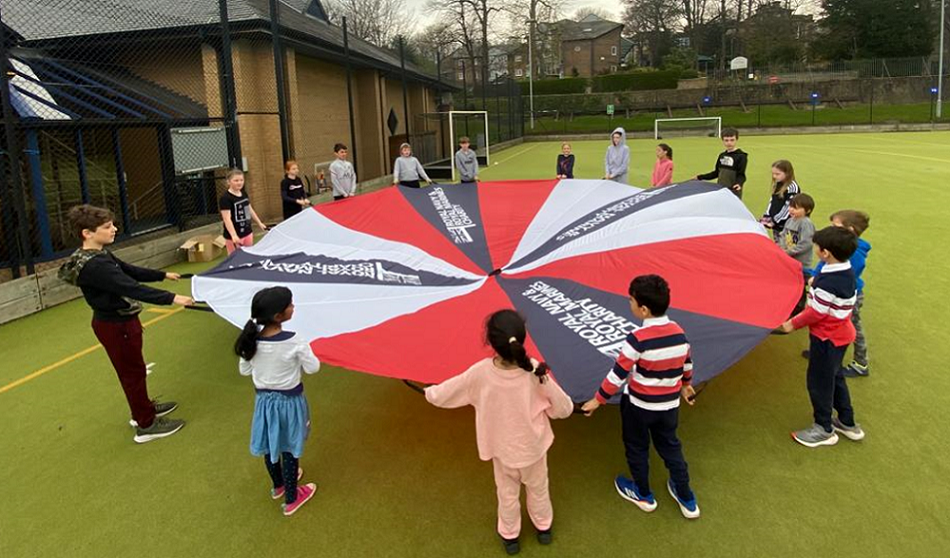 A group of children playing with a Royal Navy and Royal Marines branded parachute